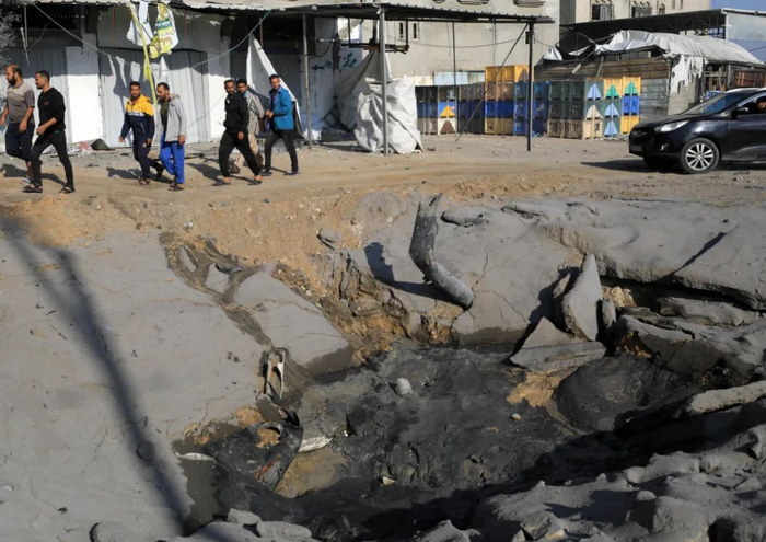 12月2日，在加沙地带南部城市汗尤尼斯，人们经过以军空袭后受损路面。新华社发（亚西尔·库迪摄）