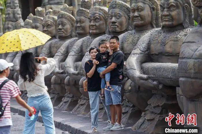 图为游客在具有东南亚民族风情的雕像前拍照。陈冠言 摄