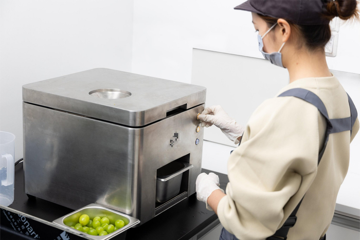 新茶饮门店店员使用自动去皮机制备青提鲜果。