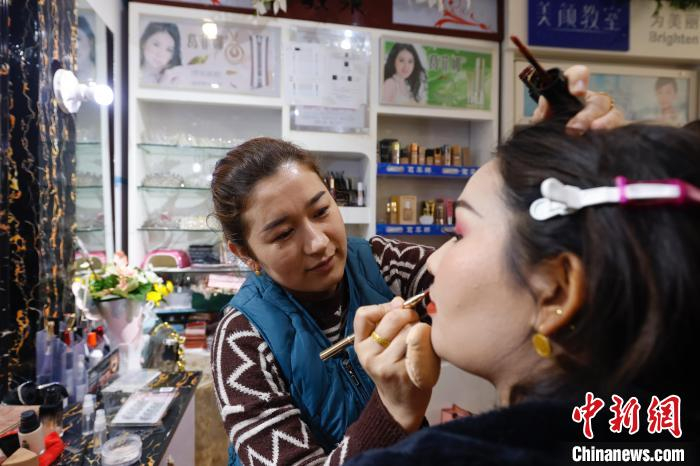 努尔比耶·阿卜杜巴柯正在给顾客化妆，2年前，她专门学习技术，从农民转型成为美容美发店老板。中新社记者 韩海丹 摄