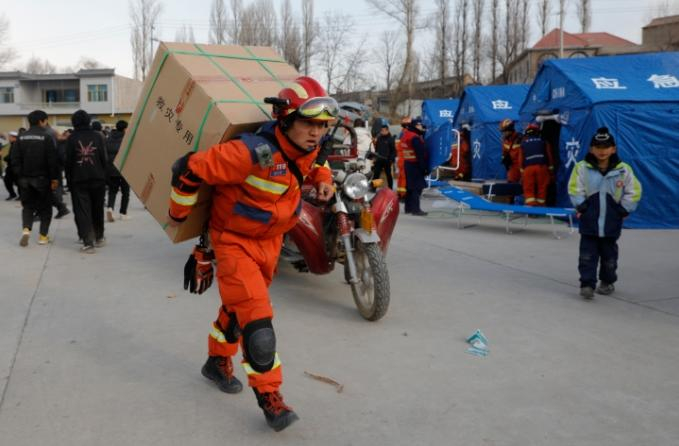 12月19日，在甘肃临夏积石山县大河家镇大河村安置点，消防人员在搬运救援物资。