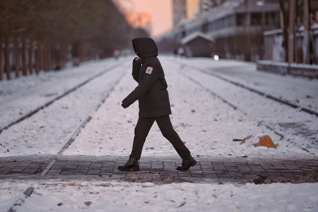 2023年12月17日，四惠，一位路人裹紧帽子防风。新京报记者 薛珺 摄