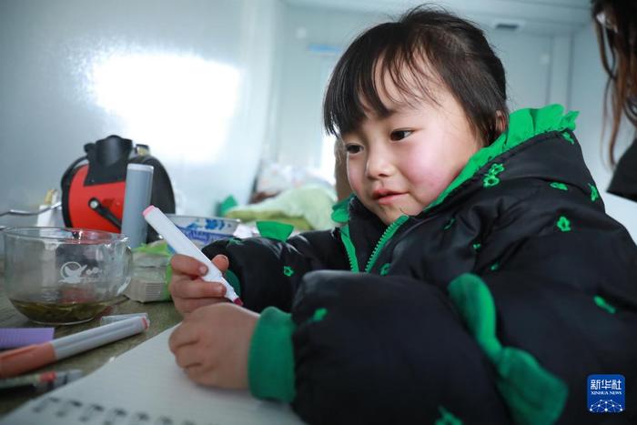 12月29日，在积石山县大河家镇大河村板房安置点，一名儿童在板房内画画。新华社记者 张睿 摄