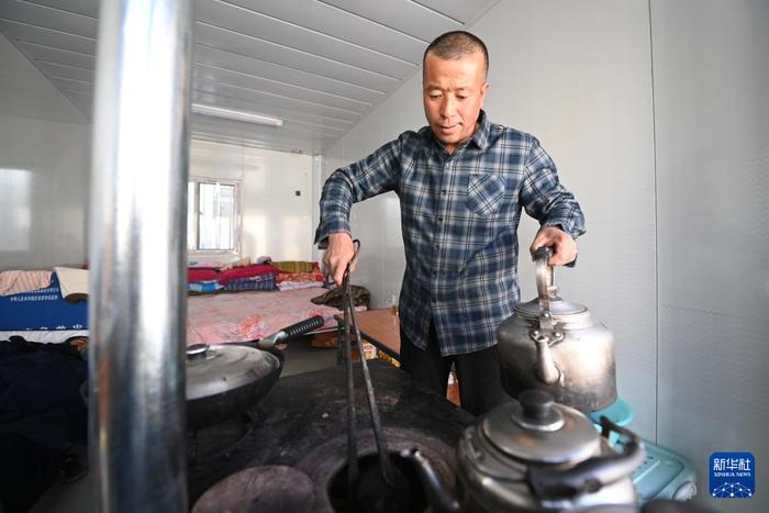 12月29日，在积石山县刘集乡高李村板房安置点，村民往火炉中加煤块。新华社记者 范培珅 摄
