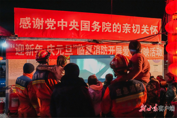 12月31日晚，甘肃省积石山县陈家村安置房区域，村民和消防员一起观看电视。辛飞 摄