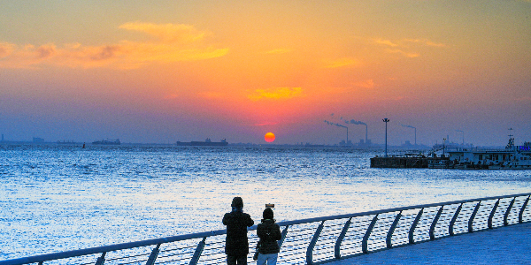 资料图：上海崇明，游人拿出手机记录下太阳缓缓落入长江的美景