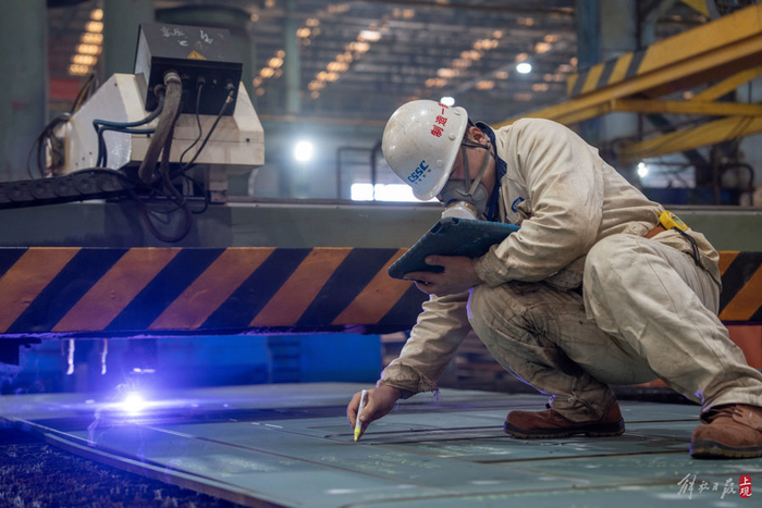 手拿电子图纸的江南造船制造一部工人正在刚切割好的零件上标注零件信息。本报记者 孟雨涵 摄