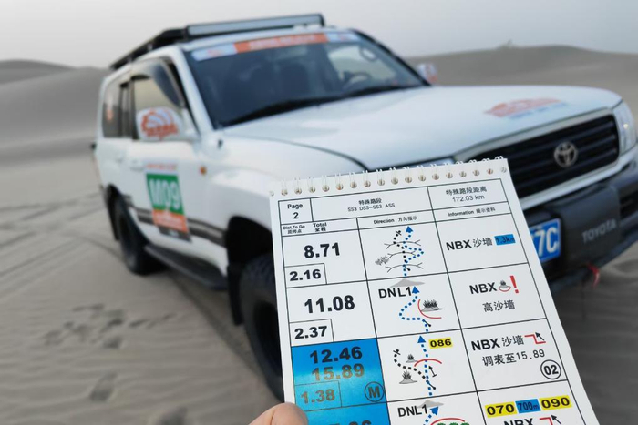 ↑2023年5月23日，新华社记者胡虎虎乘坐9号媒体越野车，手持当日比赛路书，在塔克拉玛干沙漠寻找合适点位。