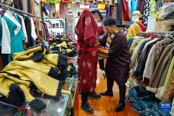 尼玛王登（右）帮助一名顾客试穿藏装（2023年12月21日摄）。新华社记者沈伯韩摄