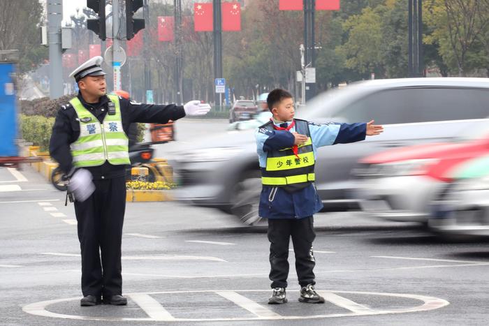 2024年1月30日，安徽省六安市裕安区解放路小学“少年警校”的队员刘雨轩（右一）跟随交警一起体验指挥交通。通讯员 摄