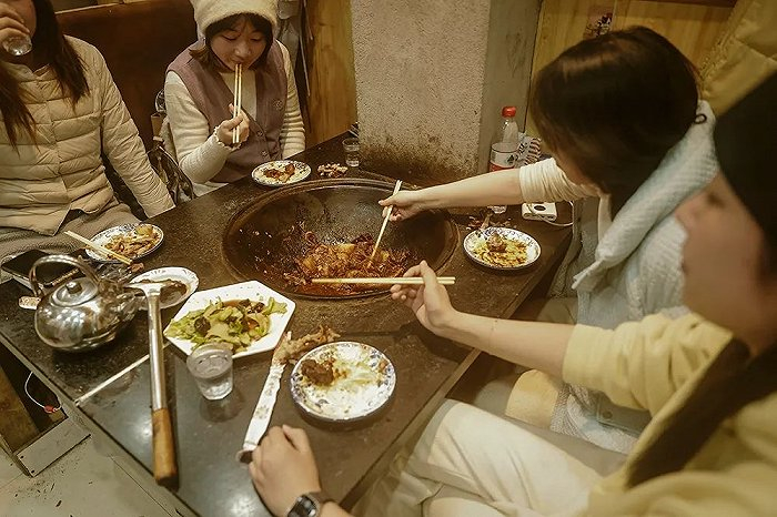 几名南方来哈尔滨旅游的姑娘一起尝试铁锅炖，这是一道具有代表性的东北菜式。