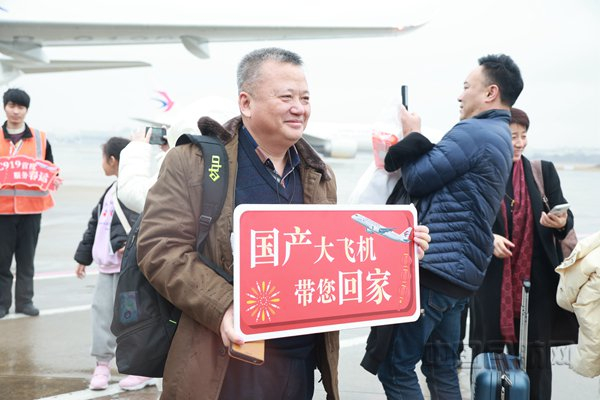 期待乘坐国产客机的旅客张先生，拿起东航准备的手牌，眼含泪花与C919合影（胡夕姮/摄）