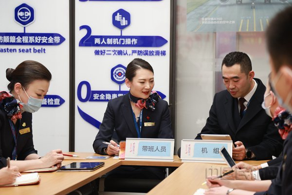 带班乘务长张璇（左二）与机长李晓亮（左三）在航前准备会上（胡夕姮/摄）