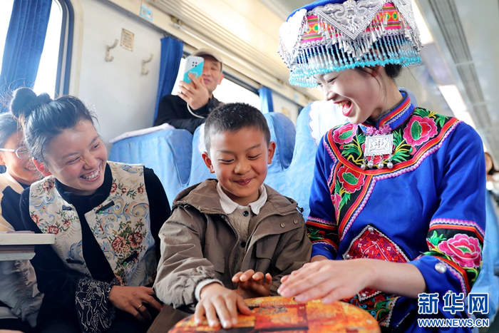昆明开往罗平的列车上，身着民族服饰的乘务员邀请小乘客体验打手鼓（摄于2月22日）。新华网发（杨紫轩 摄）
