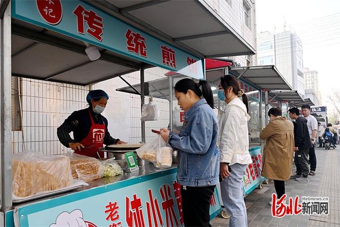 4月11日，在衡水市区康宁街与新华路路口附近的早餐“微市场”上，谢立珍（左一）正在为顾客做煎饼馃子。 河北日报记者 焦 磊摄