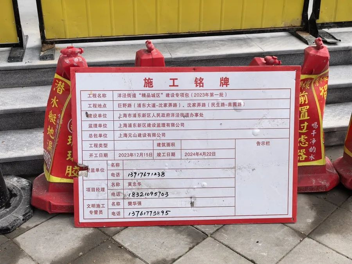 △巨野路栖山路口，一块施工铭牌倚靠在路障上。上面显示，巨野路上实施的是洋泾街道“精品城区”建设专项包。