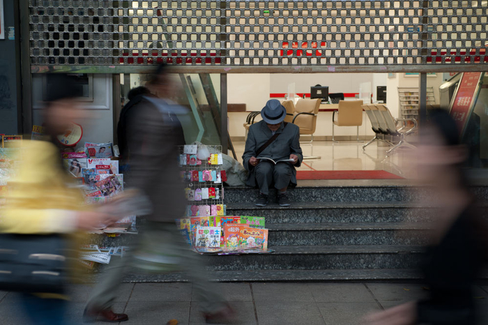 2014年4月19日，一位老人在重庆市大坪公交站的一个书摊旁阅读。