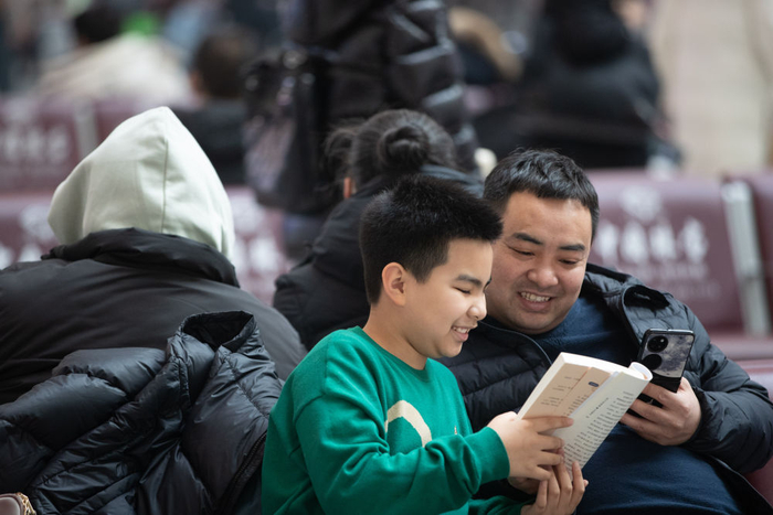 2024年1月26日，在哈尔滨火车站候车大厅，来自河北廊坊的一位小朋友（左）和父亲（右）一起读书。