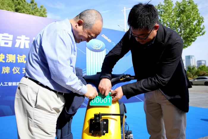 图说：中国科大副校长吴枫和阿帕科蓝集团创始人兼董事长翟光龙给Demo100项目首辆无人驾驶两轮车上“牌”
