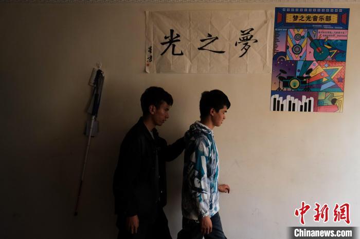 4月28日，西藏首位盲人程序员尼玛平措(右)与普琼扎西走在一幅写有“梦之光”的书法下。中新社记者 江飞波 摄