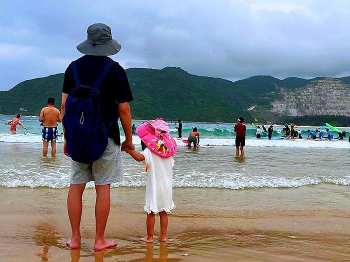 一对父女在岸边看游客冲浪、游泳（央广网记者 蔡文娟 摄）