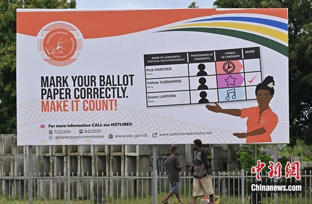 资料图：当地时间2024年4月16日，所罗门群岛首都霍尼亚拉，人们走过展示如何投票的广告牌。图/视觉中国