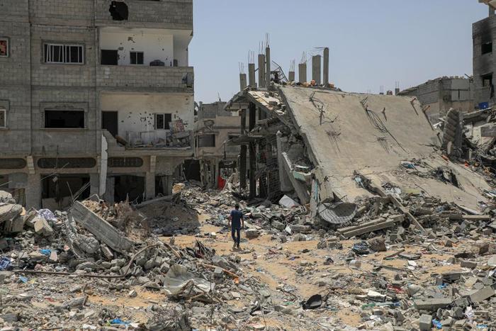 5月21日，在加沙地带南部城市汗尤尼斯，巴勒斯坦人经过以军轰炸后的废墟。（新华社发　里泽克·阿卜杜勒贾瓦德摄）