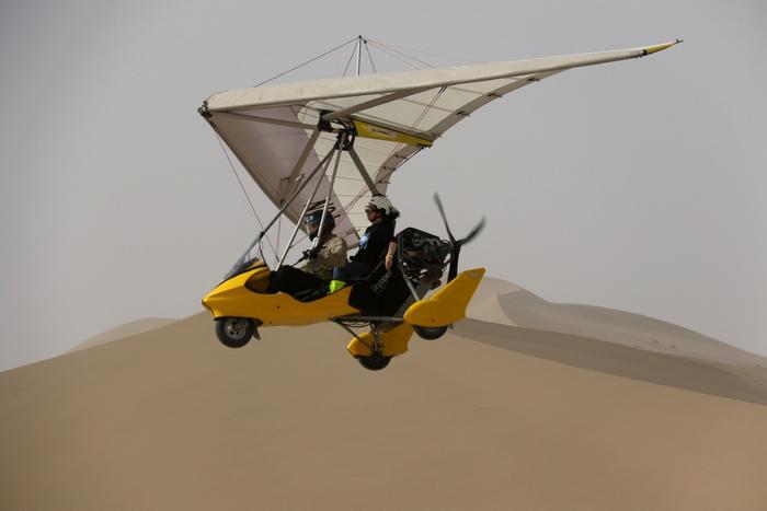 在甘肃省敦煌市鸣沙山月牙泉景区，游客乘坐动力滑翔机从空中欣赏大漠风光