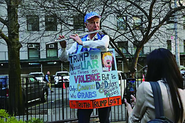     美国前总统特朗普的反对者在法庭前的公园挂着标语牌演奏乐器