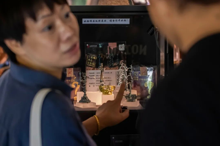 ▲6月3日，在三星堆博物馆文创店中，一名女游客向同伴介绍一号青铜神树文创产品。