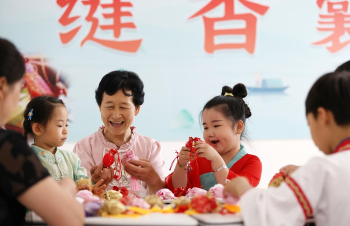 6月8日，山东省临沂市郯城县郯城街道府东社区居民为孩子讲解端午佩香囊民俗。新华社发（张春雷摄）