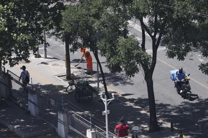6月12日中午，富丰园东路，环卫工人在烈日下清扫，一位送餐外卖员骑车驶过。  新京报记者 浦峰 摄