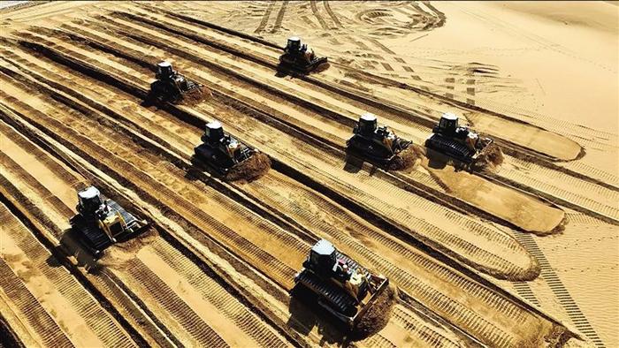 在腾格里沙漠的阿拉善盟光伏新能源+生态治理和防沙治沙光伏风电一体化项目的施工现场，百辆推土机征战腾格里沙漠。 