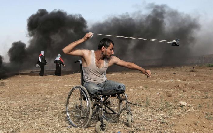 失去双腿的巴勒斯坦男子坐在轮椅上，用投石索向以军还击。图/美国广播公司