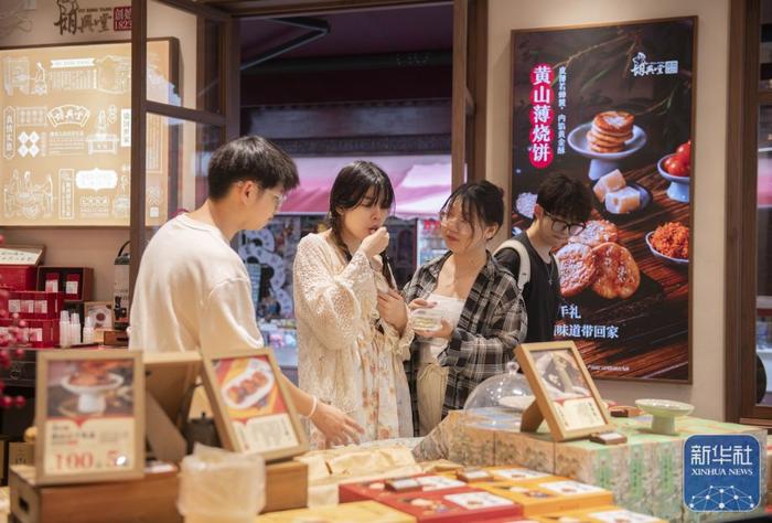 6月28日，在位于黄山市屯溪区的中国历史文化名街屯溪老街，游客在一家店铺试吃黄山特色小吃。新华社记者 傅天 摄