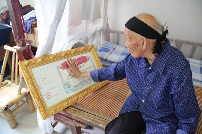   资料图：段桂秀轻抚着丈夫的烈士证明书