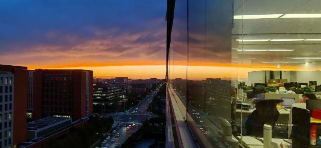 艾可在公司大楼里拍到的日落。一面是绚烂的夕阳，一面是加班的大厂人。图 / 受访者供图&nbsp;