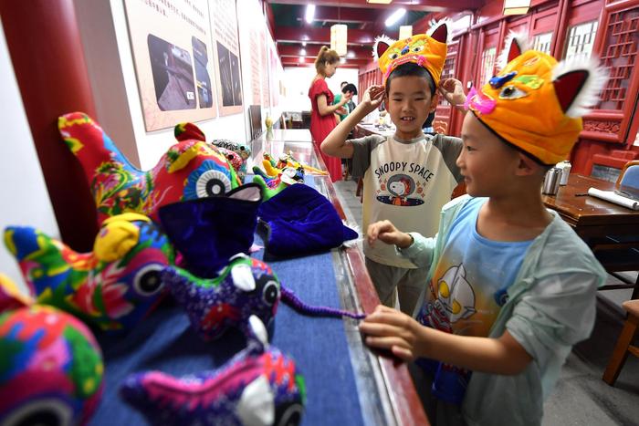 7月17日，在山东省青岛市民俗博物馆，两名小朋友在试戴非遗虎头帽。新华社