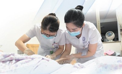 湖南株洲市中心医院田心院区综合内科护士长严碧如（左）与带教的跟班护士在患者家中做护理。本报记者申智林摄