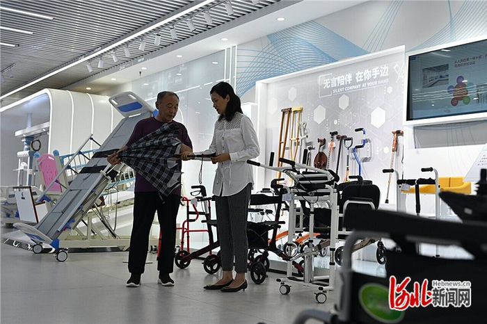 8月6日，在衡水市冀州区医疗器械和康复辅具产业发展中心，工作人员（右）向一位老年人介绍智能手杖的功能。本报记者 焦磊摄