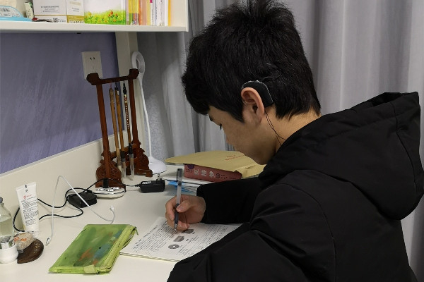 杨骐嘉在学习,他左耳做了人工耳蜗,右耳佩戴助听器。受访者供图