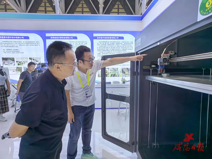 陕西金石三维打印科技有限公司销售负责人王辉（右）正在向客商展示3D打印过程。咸阳日报全媒体记者 冯晓琬 摄