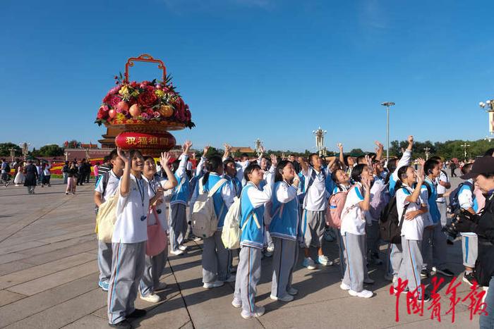 9月25日，北京天安门广场，来自北京市顺义区第十三中学的学生在“祝福祖国”巨型花篮前向高处的摄像机打招呼。王藜静/摄