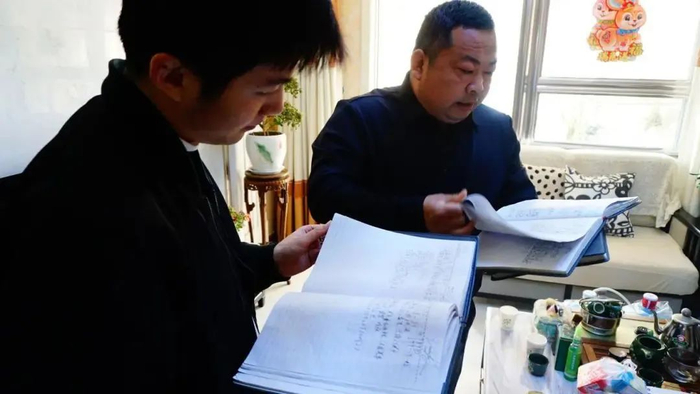 刘红涛（右）查找寻亲笔记中的资料 / 图源：中央广电总台中国之声
