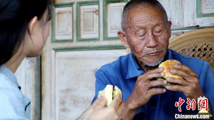 图为爷爷品尝“滇西小哥”亲手为他制作的汉堡。受访者 供图