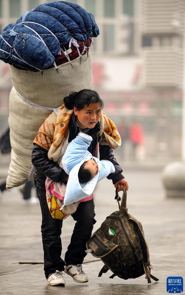 2010年1月30日，年轻的彝族母亲巴木玉布木背负超大行李、怀抱孩子在江西南昌火车站匆忙赶车。新华社记者 周科 摄