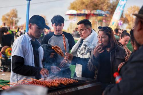 在第十四届胡杨文化系列活动美食区域，游客们徘徊在各类美食摊前，正在购买品尝各类美食。 程磊 摄