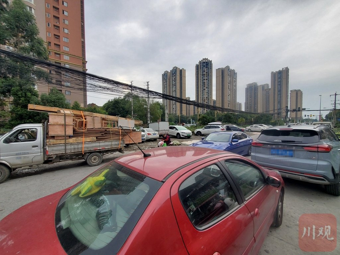 道路周边的空地上停放了许多私家车，部分车辆甚至连串停在了车道上