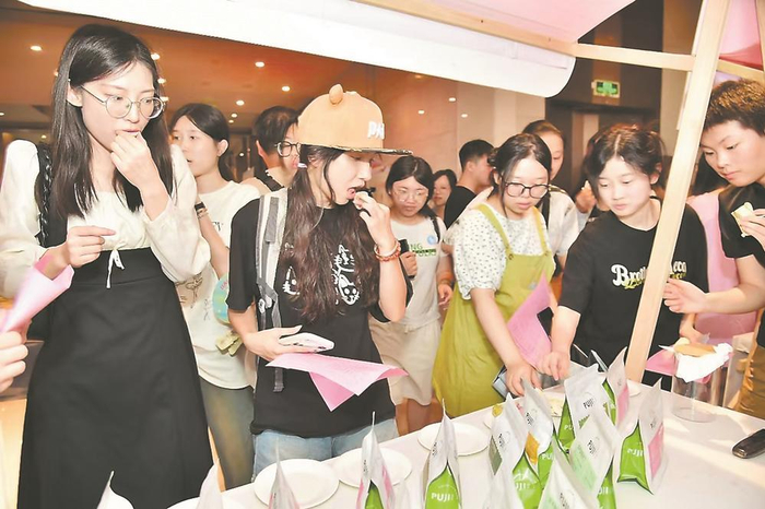       参赛师生在展位前品尝龙文本土食品企业产品。赖杰 摄