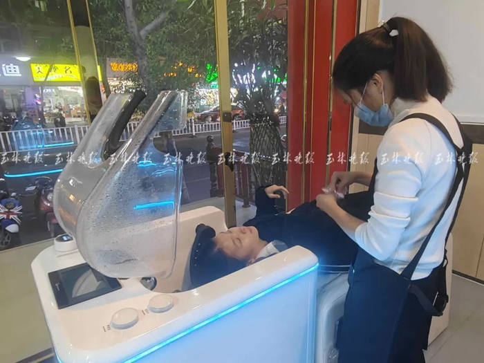 ▲店员协助顾客操作AI智能洗头机器。